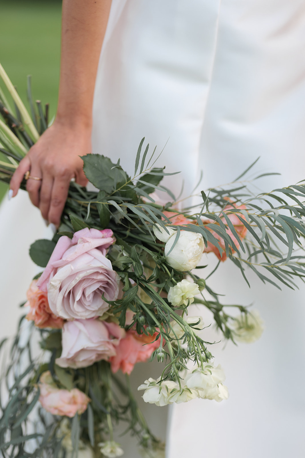 A person in a white dress holding a bouquet of assorted flowers, including pink roses and white blooms, with greenery.